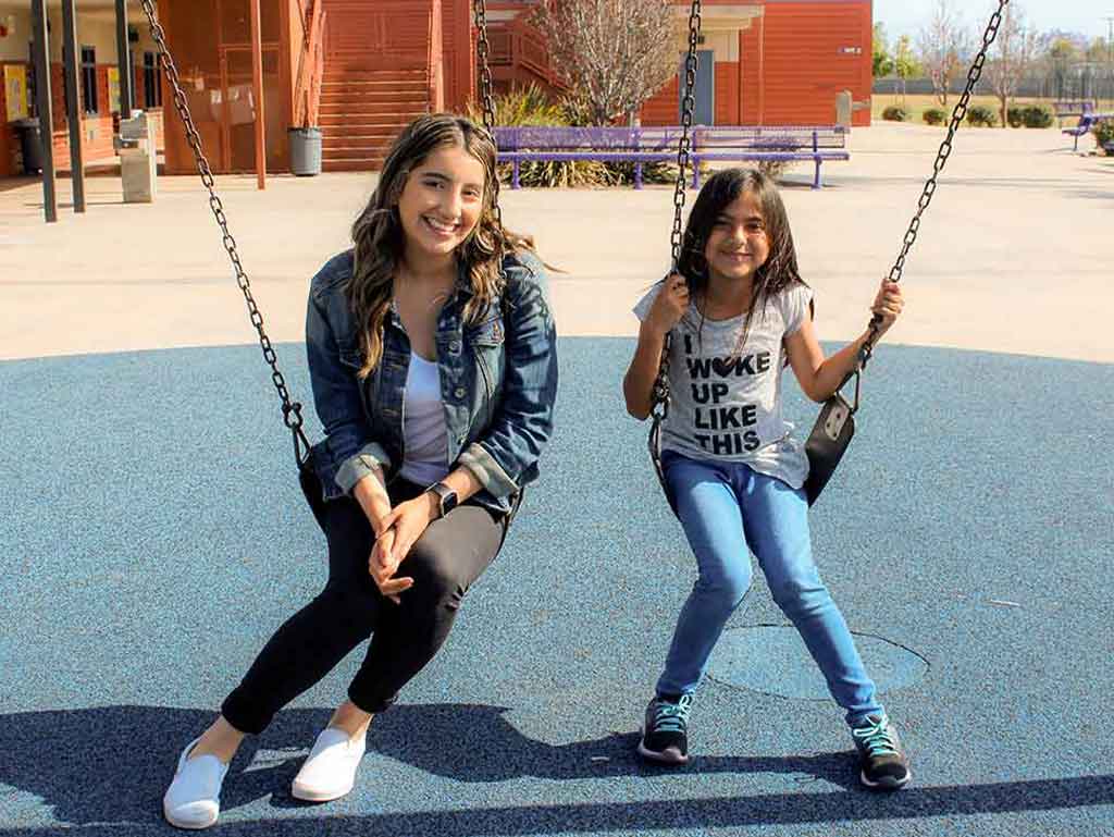 A high school mentor and her elementary school mentee swinging on the school playground